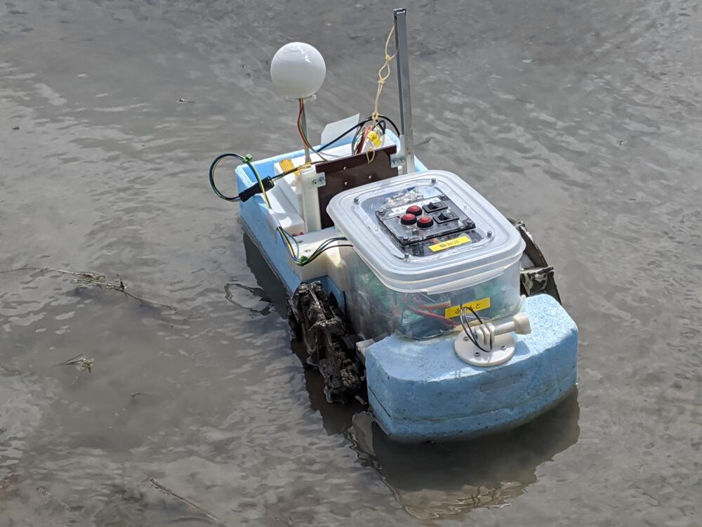 水田に浮かぶ水色の車体に黒色の車輪がついた小型ロボット